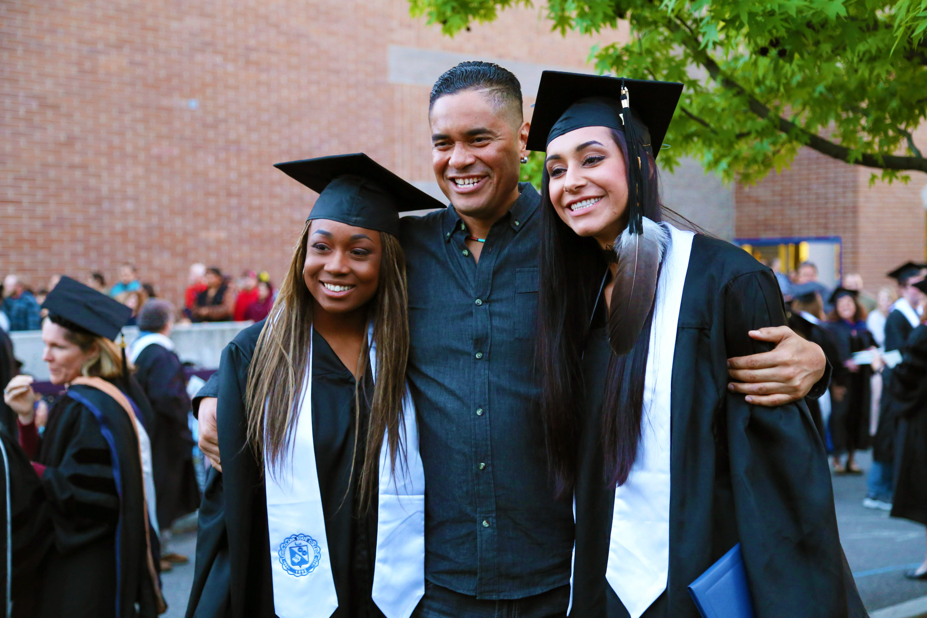 Two graduates alongside a parent at commencement