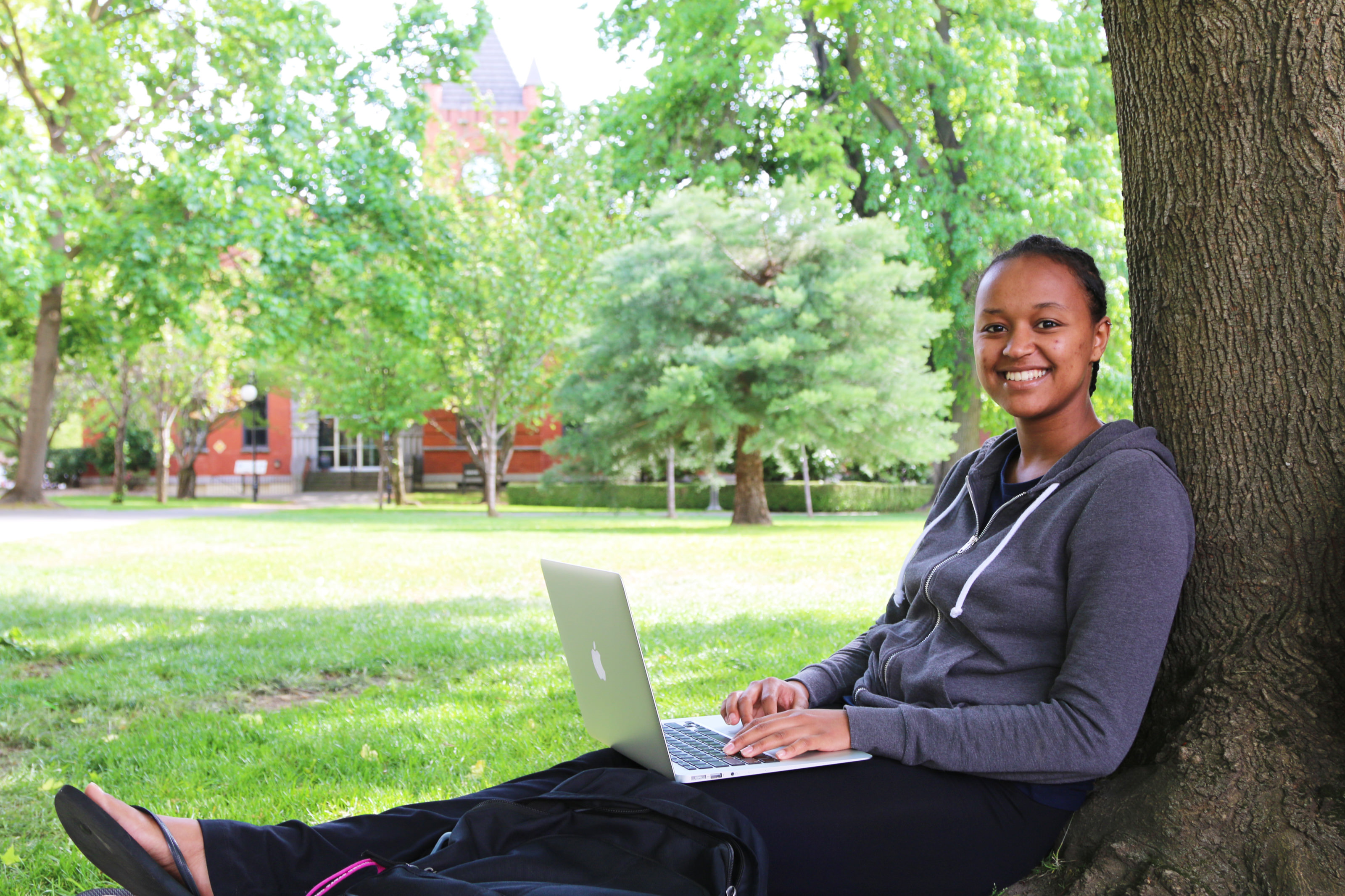 Female student sitting under a tree with a laptop on lap