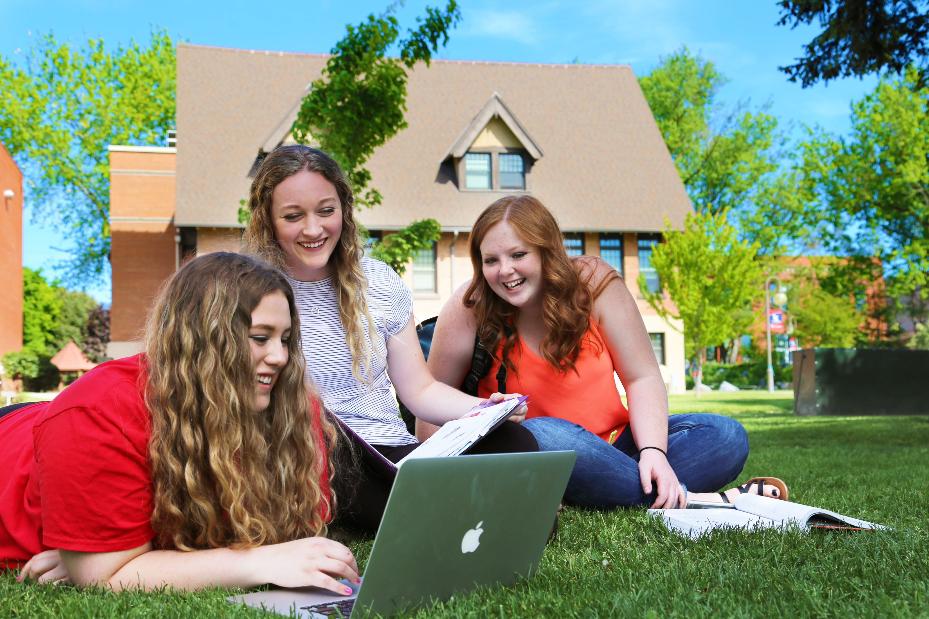Three female students sitting on grass looking at laptop