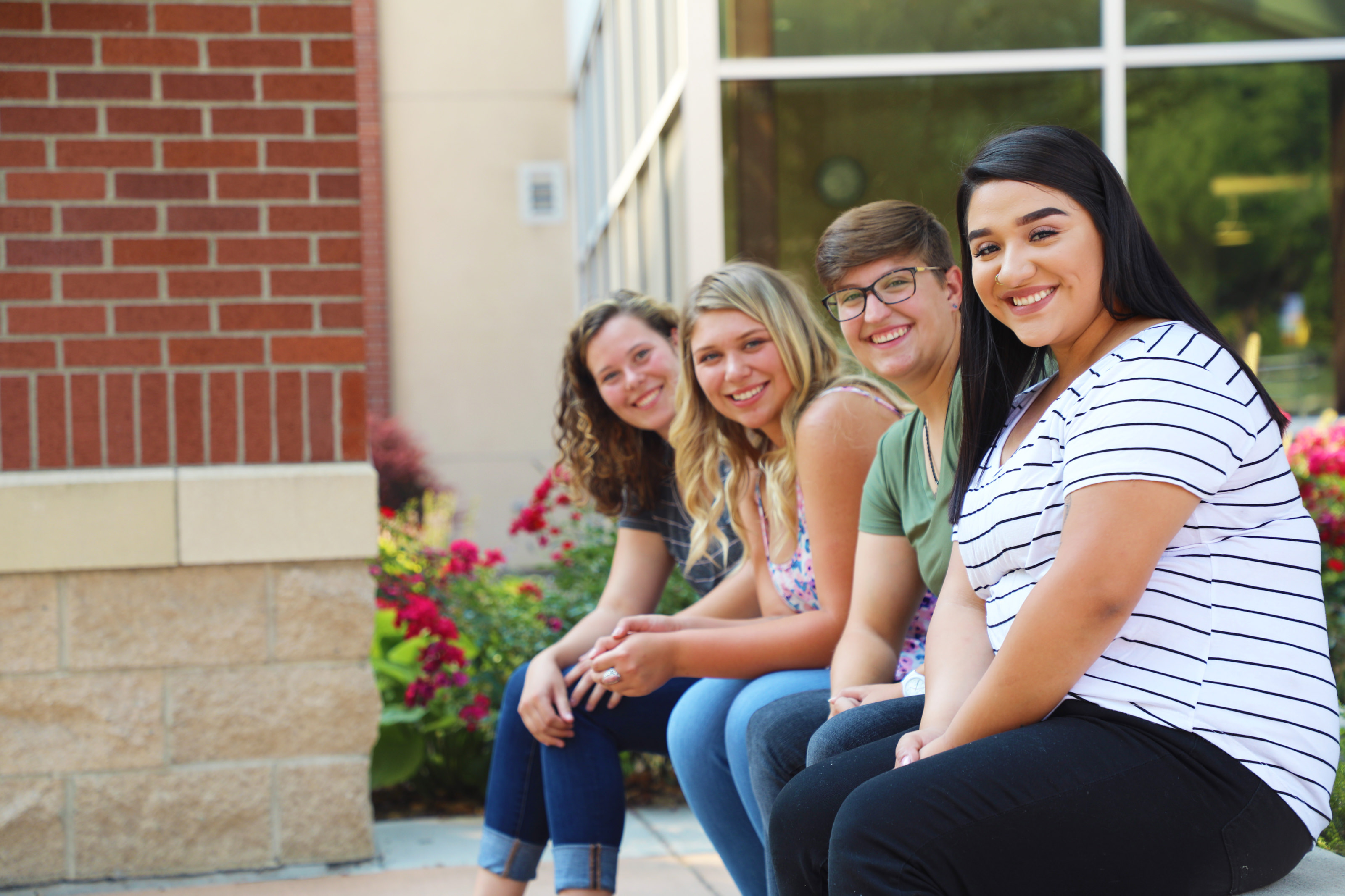 Four students sitting outside Sac Hall smiling